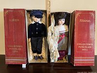 Both porcelain dolls placed standing inside their original red Alberon branded boxes showing some wear on boxes.
