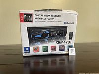 Photo of Dual car stereo model XRM47BT in original box with front panel and Bluetooth description