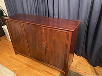 Front view of hard cherry wood credenza buffet with three closed cabinet doors and smooth top surface