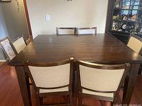 Full view of the dark hardwood dining table with six chairs, showing the cloth seats and wood grain finish.