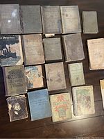 Overhead photo of 18 old books laid out on a table, showing covers and spines, all worn and fragile.