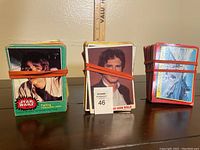 Photo of three stacks of Star Wars trading cards from 1977, 1980, and 1983 sets secured by rubber bands.