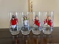 Front view of all 4 glasses featuring Popeye characters Brutus, Rough House, and two Swee Pea glasses with a ruler for scale showing about 6 inch height each.