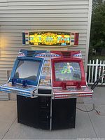 Dual-screen arcade game with blue left side and red right side controls and monitors. Red side monitor is on showing gameplay, blue side monitor is off. Marquee with boxing theme at the top.