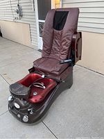 Photo of the pedicure chair showing brown padded seat and backrest, foldable armrests, remote control on seat, and whirlpool foot bath basin with footrest.