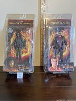 Two new in box Hunger Games action figures of Rue and Cato side by side with a ruler in the background for scale.