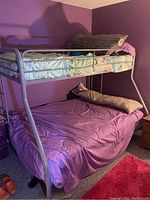 Full view of metal bunk beds with twin top and full bottom, showing bedspread, pillows, and overall frame structure.