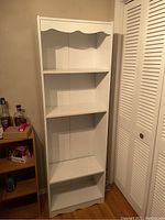 Front view of tall white bookshelf with four shelves and scalloped top edge.