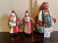 Three vintage House of Hatten Christmas ornaments: two Santas and one woman figure, with a ruler for size reference.
