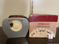 Photo showing the front of the vintage card shuffler next to the original red box with playing card graphics.