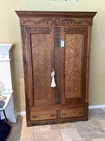 Full view of antique oak armoire showing front with double doors, scroll carved detail at top, and two drawers at bottom.