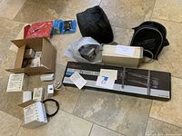 Various items laid out on floor including boxed 32-70" Rocketfish TV wall mount, APC backup battery power supply, flight gear bags, power adapters, and other electronics.