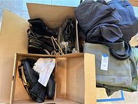Overview of box showing black flight boots, plastic hangers, folded suits and belt