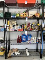 Full frontal image of the black metal 5-shelf storage rack filled with various household and automotive supplies such as motor oil, spray cans, fertilizer bags, staples, and cleaning products.