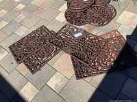 Four square decorative metal panels arranged on paver patio with a stack of circular panels in background