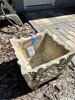 Square stone planter with scalloped edges and detailed carved lattice and leaf design, showing natural outdoor weathering. Photo taken to show design and condition.