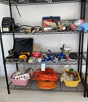 Full view of shelving unit with tools including DeWalt drill, soldering kit, wires, extension cord, valve and caulk.