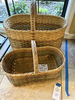 Two Tularosa baskets with woven handles and hand dyed accents, placed on a counter with sunlight.