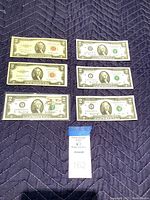 Six $2 bills including two 1953 red seal bills and four 1976 green seal bills laid out on a dark quilted surface