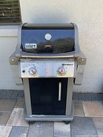 Front view of the Weber Spirit gas grill showing the lid with temperature gauge, control knobs, and lower storage area.