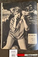 Black and white photo of Marilyn Monroe inside the magazine, showing her sitting in an outdoor setting wearing striped pants and a shirt, posing with hands near her face.