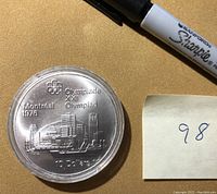 Close-up front view of the silver coin in capsule with marker pen and number card beside it.