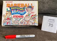 Box front with title and cartoon baseball characters, alongside red Sharpie for size reference and auction lot number.