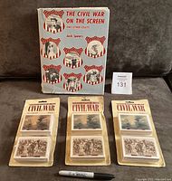 Photo shows all four items: three sealed card sets in original packaging with visible wear and writing on backs, and one oversized hardcover book with blue cover and illustrations related to Civil War on screen.