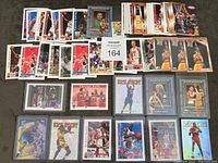 Overview of assorted basketball cards with singles and inserts laid out on floor, featuring various players and some sleeved cards.
