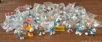 Overview of 59 bagged and loose vintage Smurfs figurines on hardwood floor