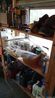 Overview of various workshop shelves showing red portable air tank, fluid containers, safety boots, goggles, and other items on wooden shelves.