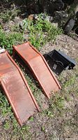Two rusted metal auto ramps and black battery chest placed on grass outdoors.