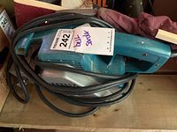 Makita electric belt sander with black power cord wrapped around the body.