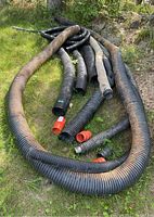 Multiple long black corrugated drainage tile pipes lying on grass outdoors, showing varying diameters and some curves in pipes.