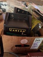 Two Zareba black metal electric fence controllers in a cardboard box labeled 'Electric Fence Supplies'.