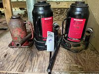 All three hydraulic bottle jacks together on a wooden surface showing condition and identification labels.