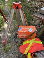 Tripod, orange hard case, and safety vest outdoors