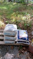 Three stacked bags of dry mason's sand and two bags of salt and sand mix on a pallet outdoors.