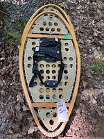 Single view of the snowshoe showing entire wooden oval frame, composite decking with circular cutouts, black binding, and metal studs on frame edge.