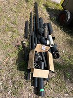 Photo of assorted black plastic plumbing pipes and fittings laid on grass with a cardboard box containing more fittings.