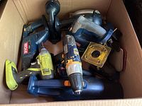 View of multiple Ryobi 18V cordless power tools including drills, sander, flashlight, handheld vacuum inside a cardboard box.