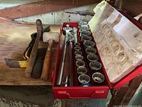 Photo showing the full set of 3/4" drive sockets and socket wrench in a red metal case alongside pry bars, hammer and mallet on a wooden surface.