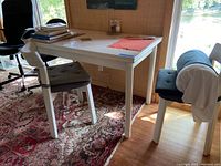 Expandable white wooden table with some items on top, set on patterned rug next to window showing natural light.