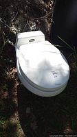 Front view of white Traveler marine toilet with closed lid outdoors.