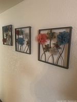 Three 3D floral metal wall art panels hanging on a wall, in a row.