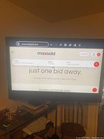 Photo of the TV turned on displaying maxsold website homepage, showing the screen is functional.