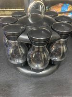 Full view of the black plastic revolving spice holder loaded with 8 clear glass spice bottles with black lids.