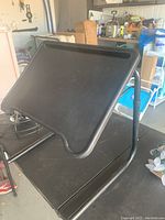 Photo showing black adjustable folding desk with slanted surface and side edge lip