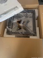 Box style light fixture wrapped in protective plastic inside packaging, showing the metal frame and bulb sockets.