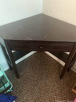 Full view of the dark brown wooden corner desk showing triangular shape, drawer, and lower shelf.
